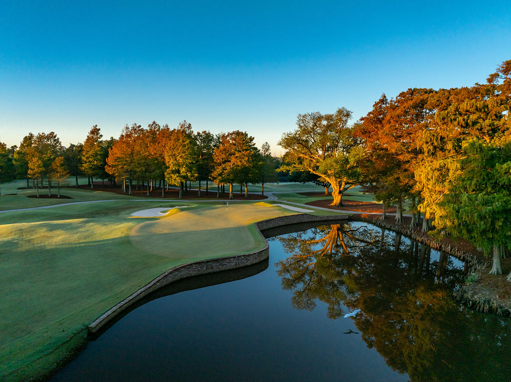 A white egret flies over the par three third hole at sunset. 